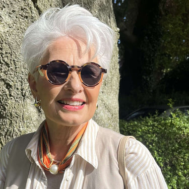 Woman wearing sunglasses and a light-colored outfit standing next to a tree