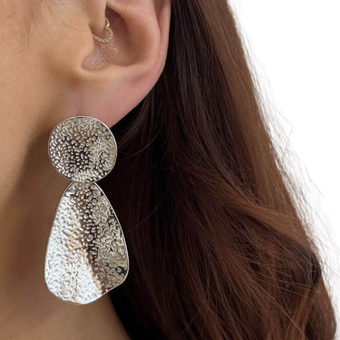 Silver earrings worn by a person with brown hair.