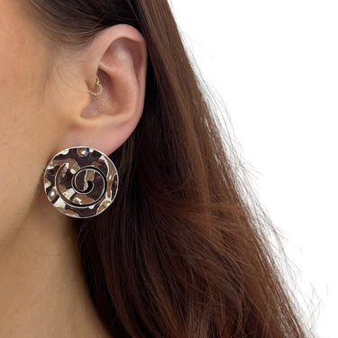 Close-up of a person wearing a round silver earring with a design.