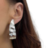 Close-up of a person wearing a silver hoop earring with a textured design.