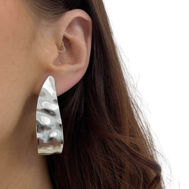 Close-up of a person wearing a silver hoop earring with a textured design.