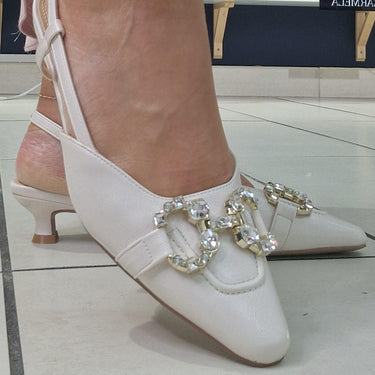 cream shoes with decorative elements worn by a person in a pink skirt, on a tiled floor.