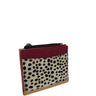 A small zippered card holder or wallet featuring a dalmatian print hair-on-hide front panel, a burgundy leather top section, and tan leather trim, shown on a plain white background.