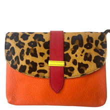 Leopard print clutch with orange base and red strap on a white background