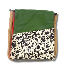 A square patchwork leather bag by senika, featuring a green leather top flap, a black and white cow-print patterned panel, tan leather sides, and a red leather accent strip.