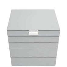 A light gray jewelry box with a hinged lid and four drawers, featuring a small silver metal brand plaque on the front.