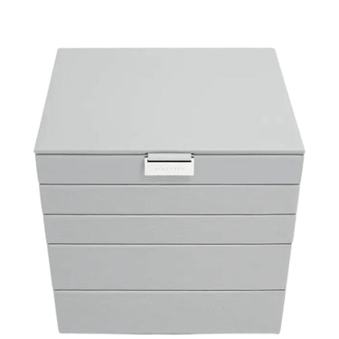 A light gray jewelry box with a hinged lid and four drawers, featuring a small silver metal brand plaque on the front.