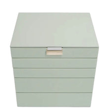 A square jewelry box with a hinged lid and five horizontal drawers, finished in a pale sage green color with a small beige brand plaque on the front.