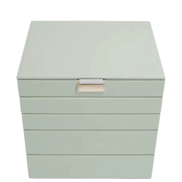A square jewelry box with a hinged lid and five horizontal drawers, finished in a pale sage green color with a small beige brand plaque on the front.