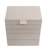 A square jewelry box in a light taupe-beige faux leather finish with a small gold-tone metal accent on the front, shown on a plain white background.