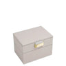 A rectangular two-tier jewelry box in a light taupe textured material, featuring a small gold-tone metal clasp on the front, set against a plain white background.