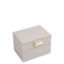 A rectangular two-tier jewelry box in a light taupe textured material, featuring a small gold-tone metal clasp on the front, set against a plain white background.