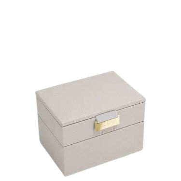A rectangular two-tier jewelry box in a light taupe textured material, featuring a small gold-tone metal clasp on the front, set against a plain white background.