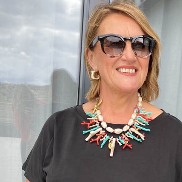 Woman wearing a black top and colorful necklace standing in front of a glass door.