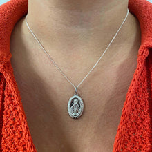 Silver necklace with a pendant worn by a person wearing an orange sweater.