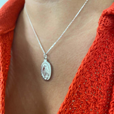 Silver necklace with a pendant worn by a person in an orange garment