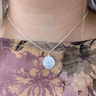 Silver necklace with a round pendant worn by a person against a floral background