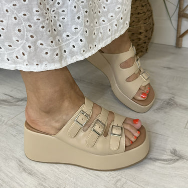 Beige platform sandals worn with a white dress on a light wooden floor.