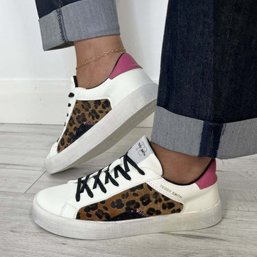 White sneakers with leopard print soles worn by a person on a light wooden floor.
