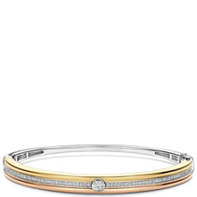 A two-tone bangle bracelet featuring a polished gold band, a rose gold band, and a channel-set row of clear stones. A round-cut clear stone is set in the center, with the bracelet photographed on a clean white background.