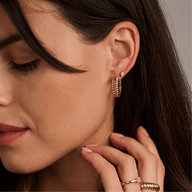 Close-up of a woman wearing gold hoop earrings with a neutral background