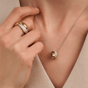 Close-up of a hand adjusting a gold necklace with a pendant on a beige background