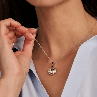 Person wearing a silver necklace with a shell pendant, held by another person.