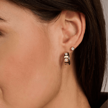 Close-up of an ear wearing a gold hoop earring with small diamonds.