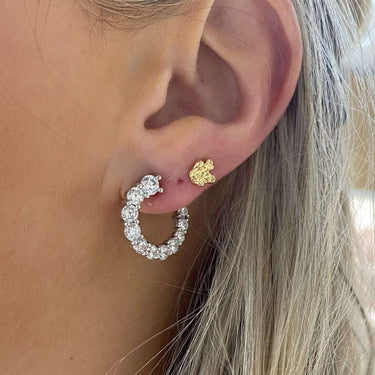 Close-up of an ear wearing a silver hoop earring with a gold heart charm.