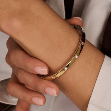 Gold bangle with small diamonds on a wrist against a neutral background