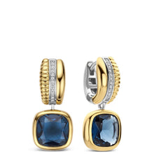 A pair of gold and silver hoop earrings with a large blue cushion-cut gemstone dangling below, shown on a clean white background.