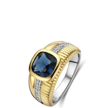 A two-tone ring featuring a cushion-cut dark blue gemstone in a gold bezel setting, with a textured gold band accented by a channel of small clear stones and a polished silver-toned band.