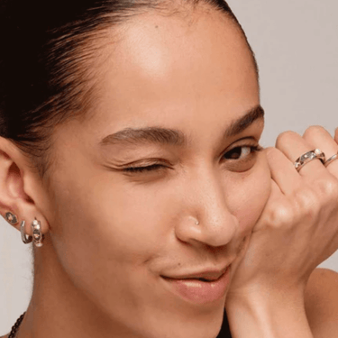 Close-up of a person wearing earrings and a ring, with a neutral background