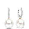 A pair of drop earrings featuring large white freshwater pearls suspended from silver huggie hoops adorned with pavé-set clear cubic zirconia and gold accents.
