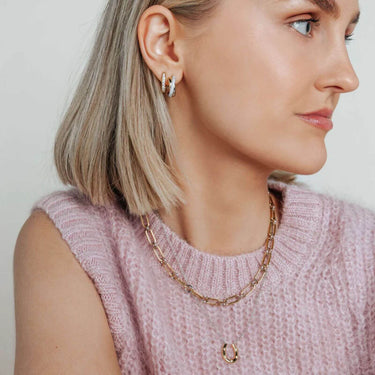 Woman wearing a gold chain necklace and hoop earrings against a neutral background