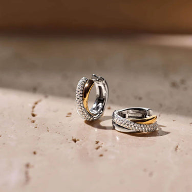 Pair of silver hoop earrings with gold accents on a textured surface