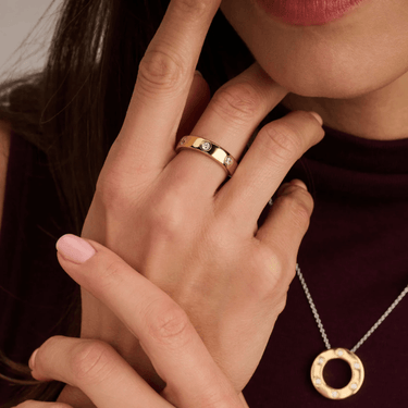 Close-up of a person wearing a gold ring and necklace, with one hand covering the other.
