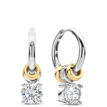 A pair of small hoop earrings with a dangling solitaire diamond and gold and white gold accents, shown on a plain white background.