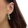 Close-up of an ear wearing a turquoise hoop earring with gold accents.