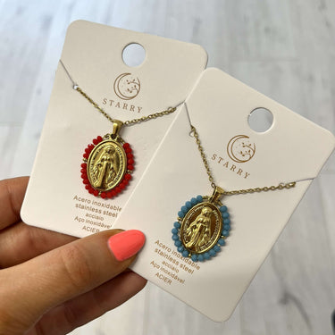 Two necklaces on display cards held by a hand with pink nail polish.