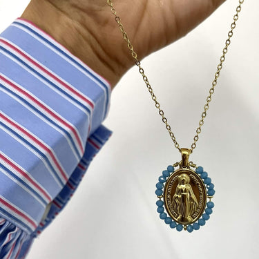 Gold necklace with a pendant held by a person wearing a striped shirt on a white background