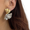 Close-up of a person wearing gold and silver leaf-shaped earrings.