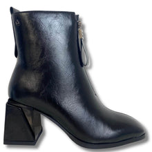 A black faux-leather ankle boot with a chunky geometric block heel, a pointed toe, and a side zipper with a decorative pull tab, shown against a plain white background.