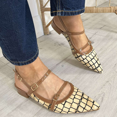 Person wearing gold and brown strappy flats with blue jeans on a light wooden floor.