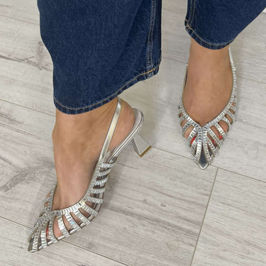 Silver strappy high-heeled shoes worn with blue jeans on a wooden floor.