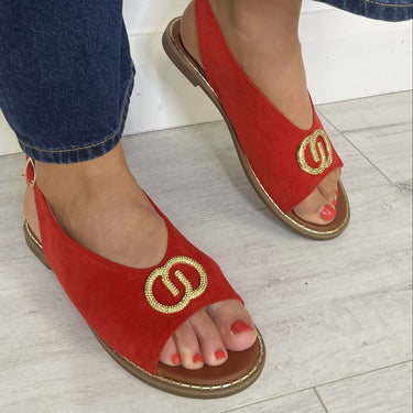 Red sandals with gold logo worn with blue jeans on a light wooden floor.