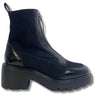 A black ankle boot with a chunky platform sole, featuring a mix of matte suede and glossy patent leather panels, shown against a plain white background.