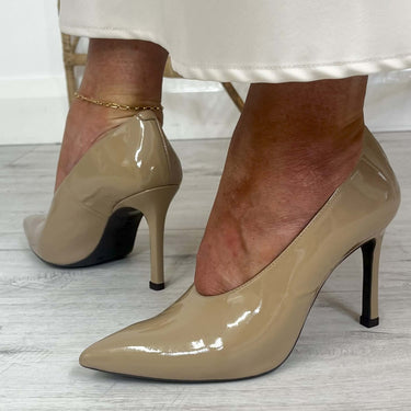 Beige patent high-heeled shoes worn by a person on a light wooden floor.