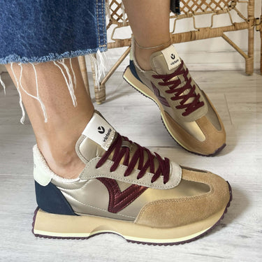 Beige and maroon sneakers worn with a denim skirt on a light wooden floor.