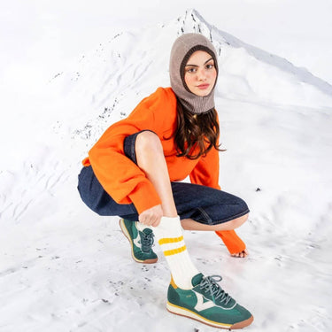 Person wearing an orange sweater, denim pants, and green shoes in a snowy setting